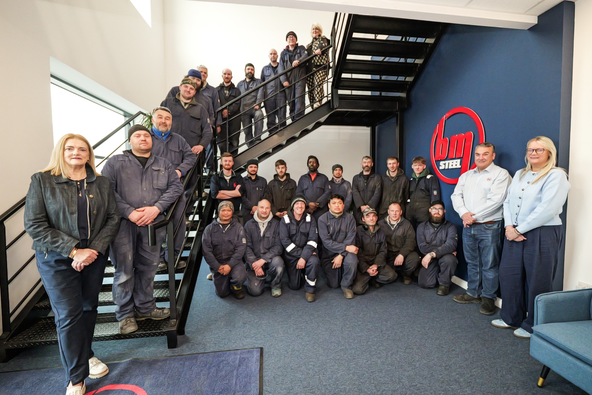 The wider BM Steel team gathered beside the BM logo in Newry